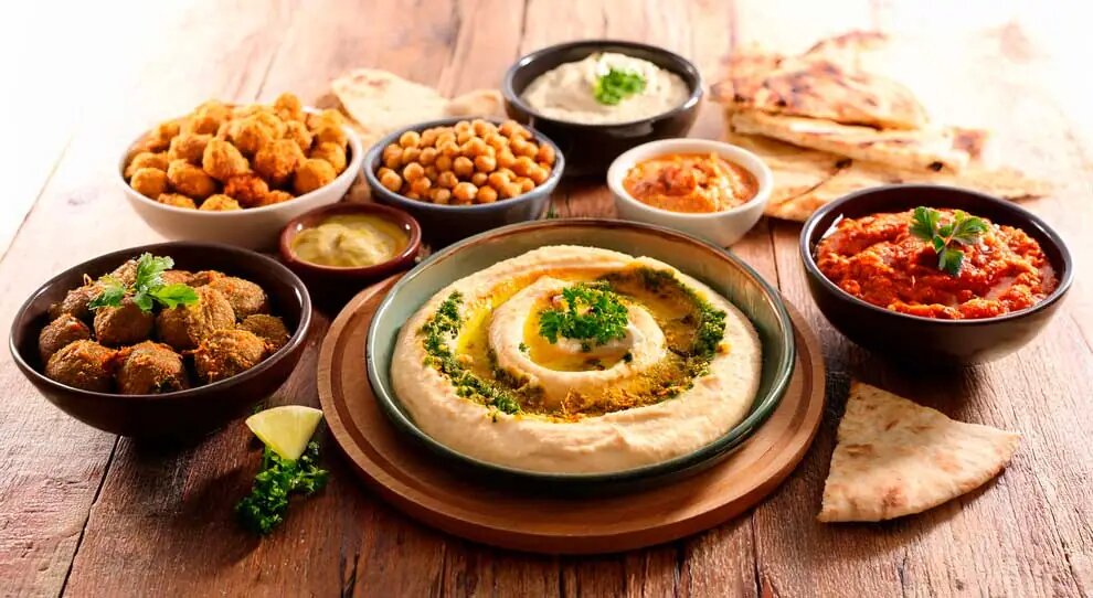 Mesa de culin&aacute;ria &aacute;rabe da YOFAH para eventos, com hommus, kibes, gr&atilde;o-de-bico e p&atilde;es